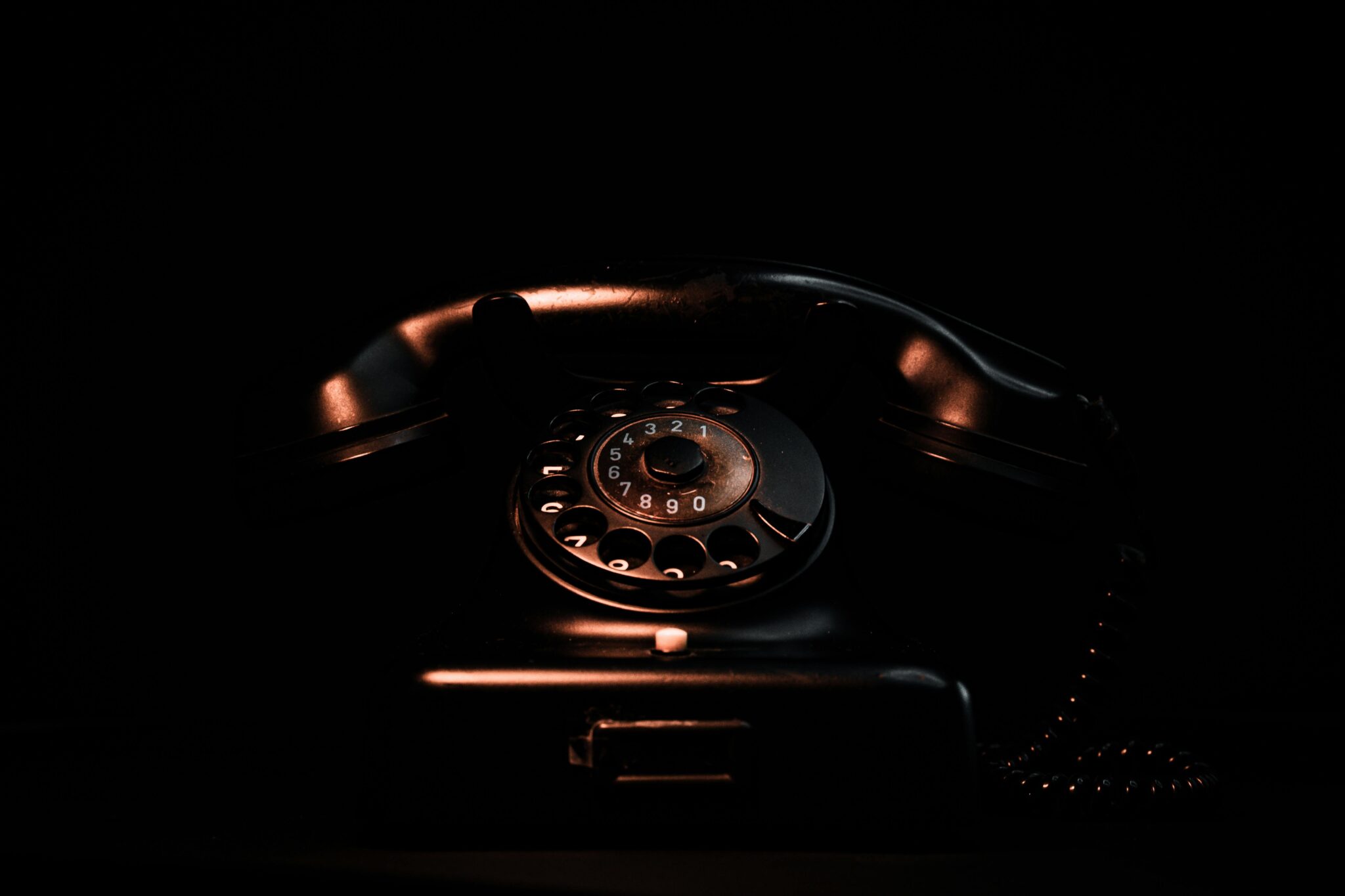 Vintage black rotary phone in a dark setting highlighting its classic design and retro appeal.